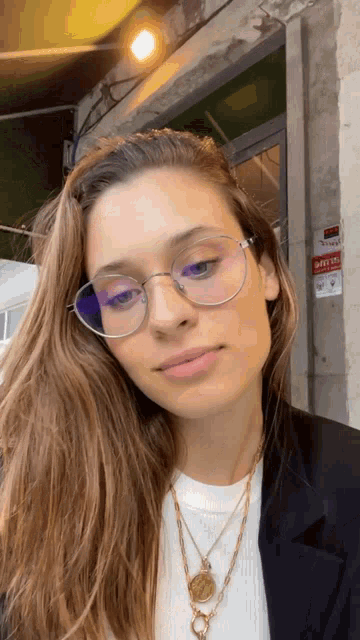 a woman wearing glasses and a necklace is standing in front of a building that has a sign on it that says safety