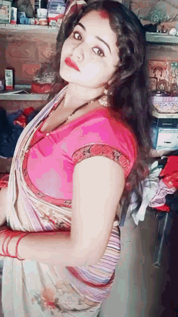 a woman in a saree and a pink top is standing in a room .