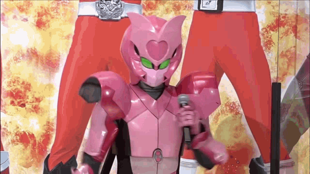a pink robot with green eyes is holding a microphone in front of a man in red pants