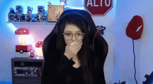 a woman wearing headphones and glasses covering her mouth in front of a stop sign that says alto