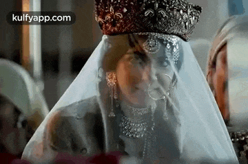 a woman wearing a veil and a crown is standing in front of a group of people .
