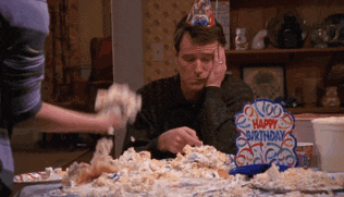 a man wearing a party hat sits at a table with a birthday cake