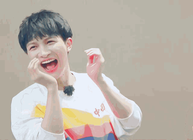 a young man wearing a white shirt with a yellow stripe is laughing with his mouth open