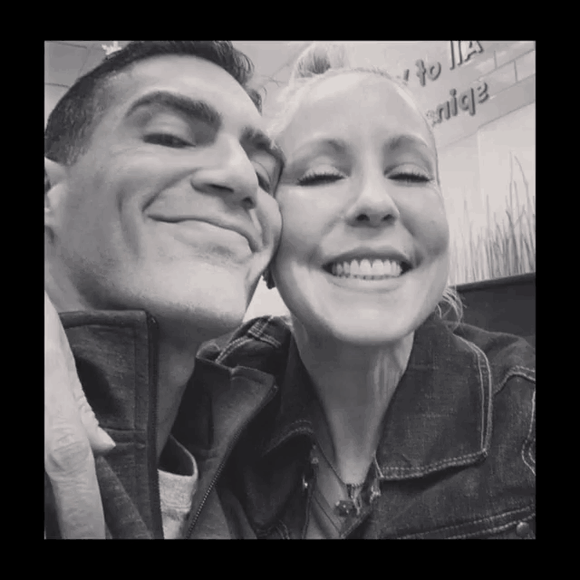 a black and white photo of a man and a woman smiling in front of a sign that says " nice "