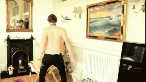 a shirtless man is dancing in a living room in front of a painting