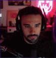 a man with a beard wearing headphones is sitting in front of a computer screen .
