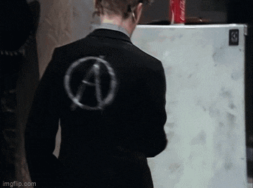 a man in a suit with an anarchy symbol on his back is standing in front of a white refrigerator .