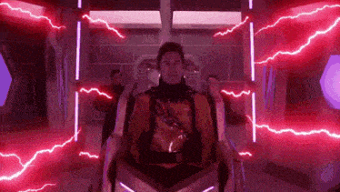 a man is sitting in a futuristic chair with red lightning coming from the ceiling .