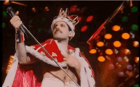 freddie mercury is wearing a crown and holding a microphone on stage .