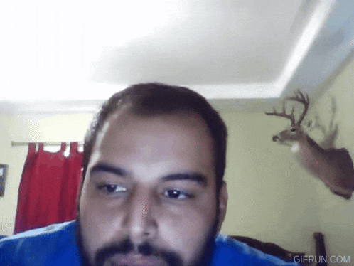 a man with a beard is looking at the camera in front of a deer head mounted on the wall