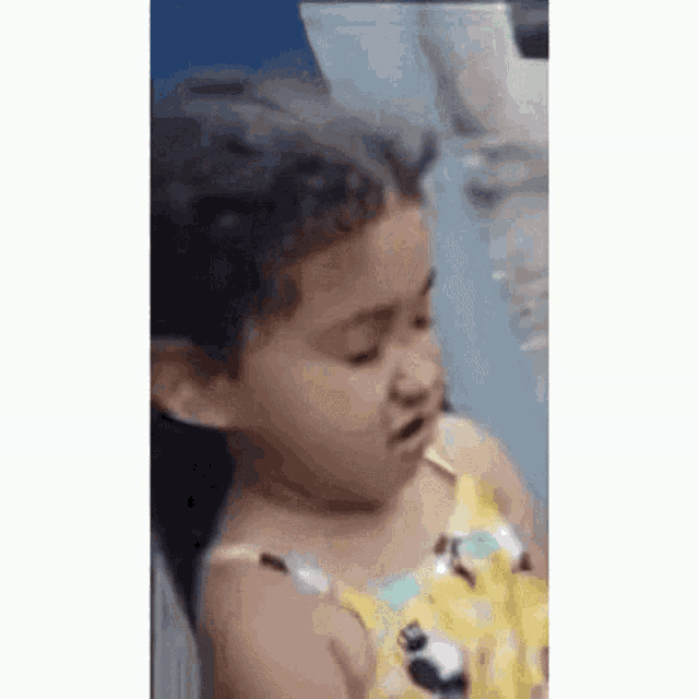 a little girl in a yellow dress is making a funny face while sitting in a chair .