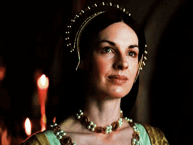 a woman wearing a green and gold dress and pearls looks to the side