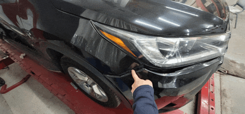 a person pointing at a black car 's front bumper