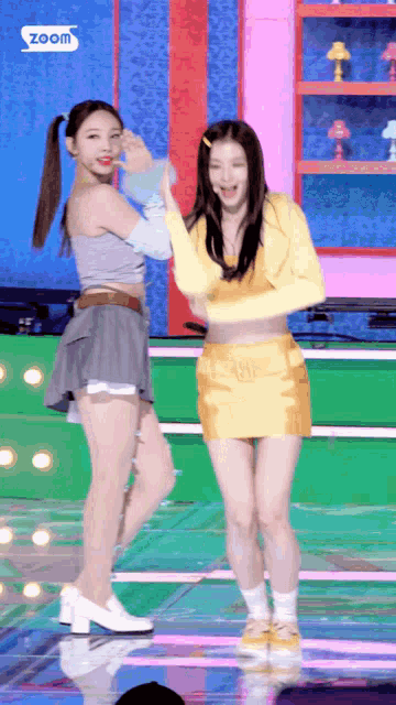 two women are dancing on a stage and one is wearing a yellow skirt and a gray top .