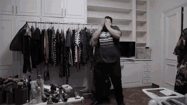 a man standing in front of a rack of clothes covering his face with his hands