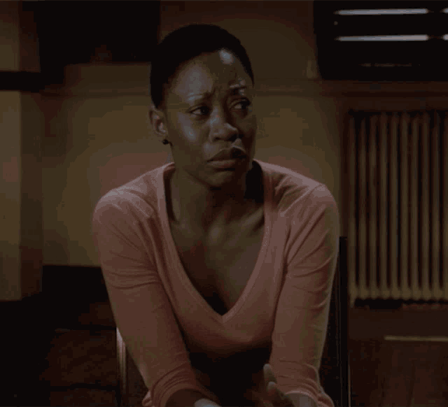 a woman in a pink shirt sits in a chair with her hands folded