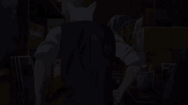 a man in a black vest is standing in a dark room with boxes in the background