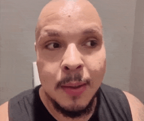 a bald man with a beard is making a funny face while wearing a black tank top .