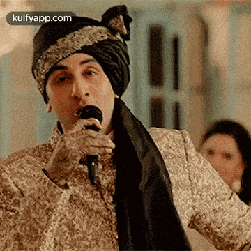 a man in a turban is singing into a microphone while wearing a suit .