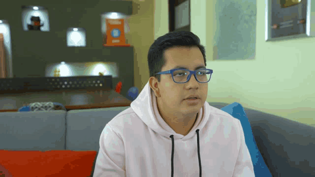 a young man wearing glasses and a pink hoodie sitting on a couch