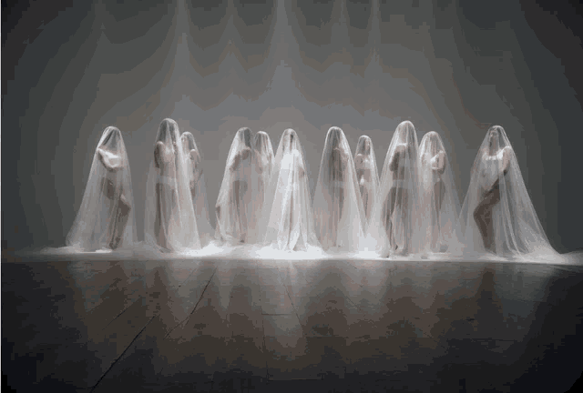a group of women are standing in a row covered in white sheets