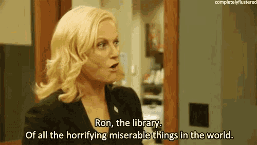 a woman in a black suit is talking to a man in a library .