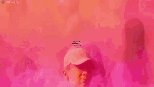 a man in a hat is taking a picture of himself with a cell phone in front of a pink background .