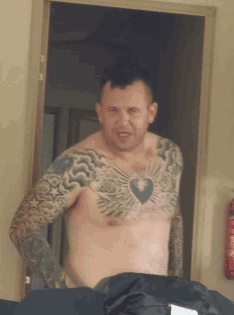 a shirtless man with a tattoo on his chest stands in a doorway