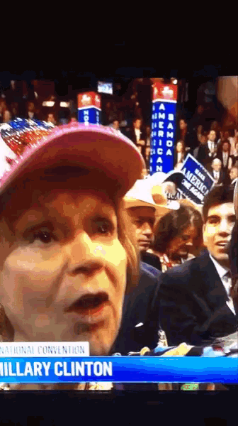 a woman wearing a red hat stands in front of a banner that says national convention hillary clinton