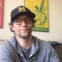 a man wearing glasses and a black hat with the letter m on it