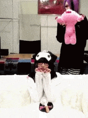 a girl in a cat hat is sitting on a bed holding a pink stuffed animal .