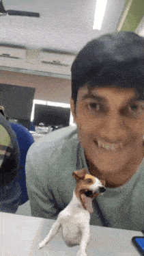 a man is sitting at a table with a small dog that is sticking its tongue out