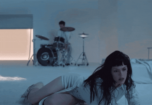 a woman is laying on the floor with a drummer in the background