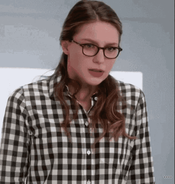 a woman wearing glasses and a plaid shirt is making a funny face .