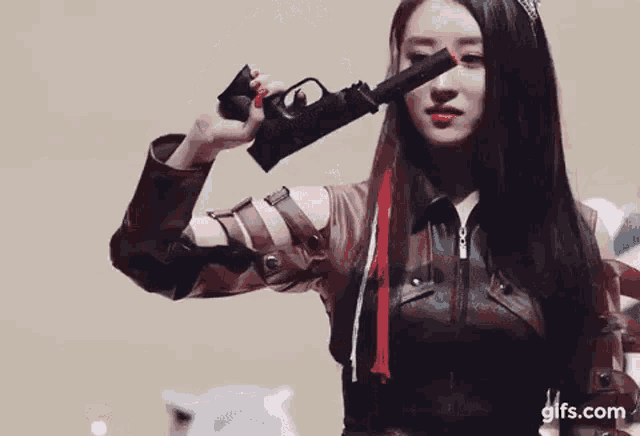 a woman in a leather jacket is holding a gun behind her head .