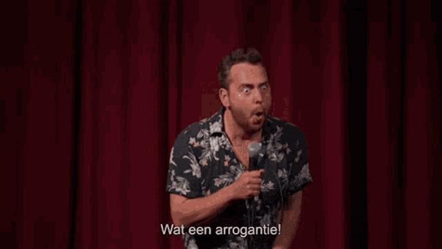 a man is holding a microphone on a stage and says wat een arrogantie .