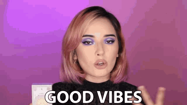 a woman with pink hair and purple eyeshadow is holding a box and saying good vibes .