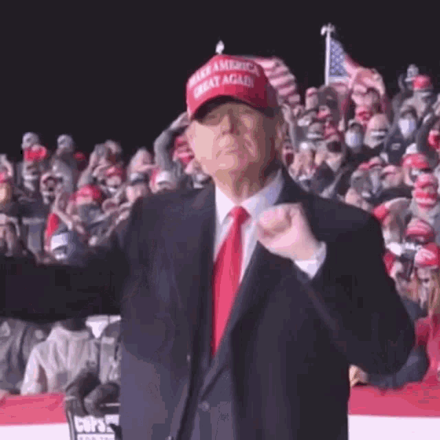 donald trump is wearing a red hat and gloves while giving a thumbs up at a rally .