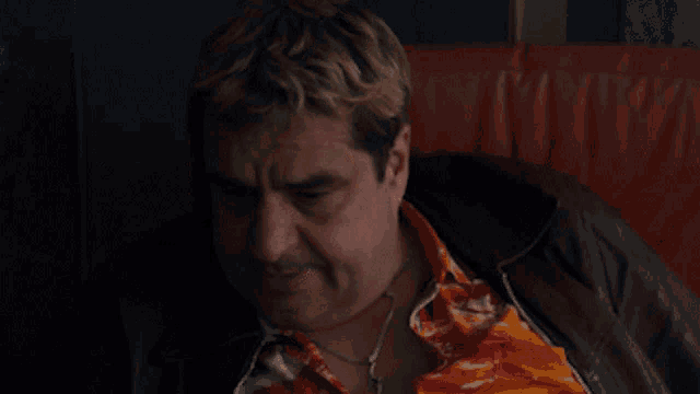 a man wearing a leather jacket and a colorful shirt is sitting on a couch