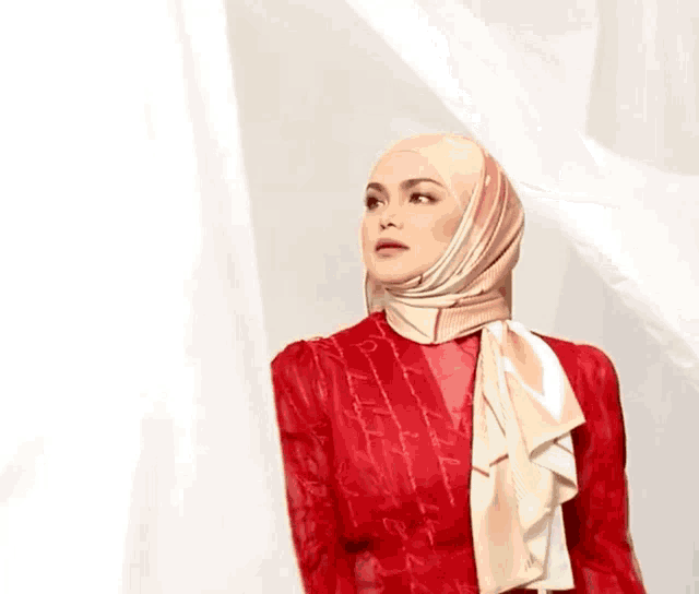 a woman wearing a hijab and a red dress stands in front of a white background