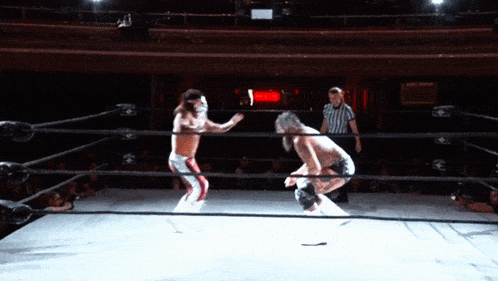 two men are wrestling in a ring with a referee in the corner