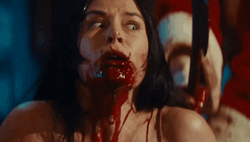 a woman with blood coming out of her mouth is being tortured by a man wearing a santa hat .