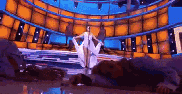 a woman in a white dress is singing into a microphone on stage