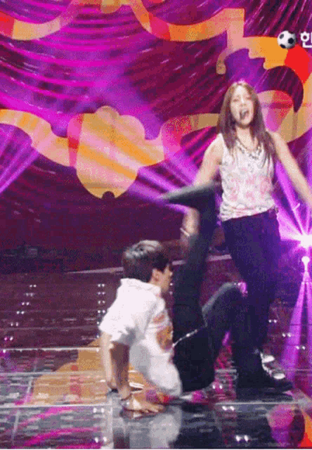 a woman is standing on a man 's back on a stage with a soccer ball in the background