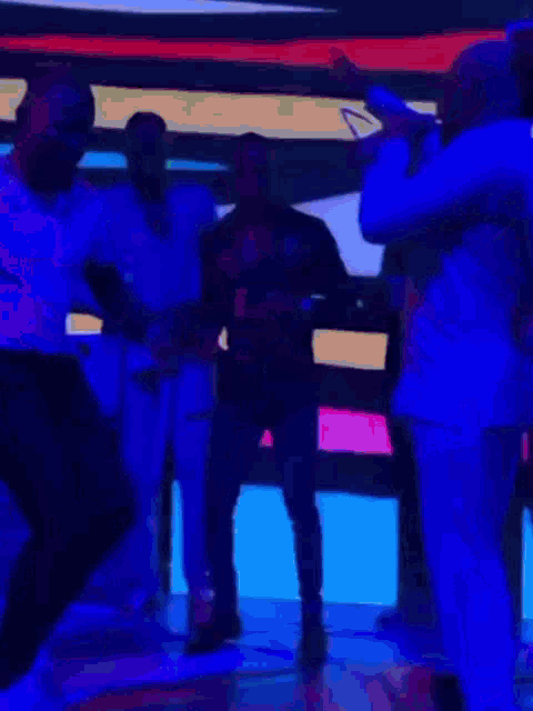 a group of people are dancing on a stage with blue lights behind them