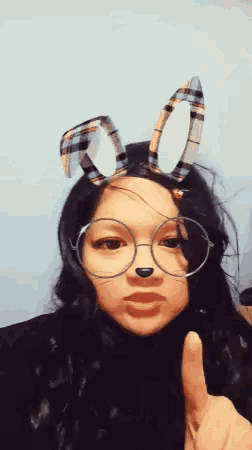 a girl wearing glasses and plaid bunny ears giving a thumbs up