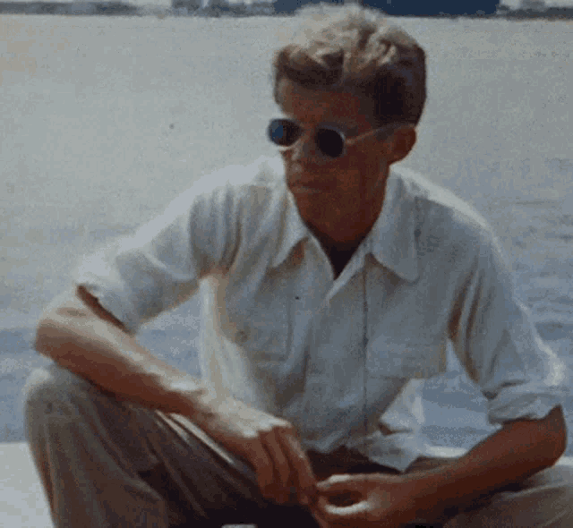 a man wearing sunglasses and a white shirt sits in front of the water