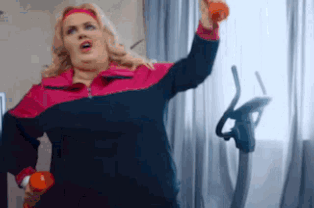 a woman is holding a dumbbell and a bottle of water while standing in front of an exercise bike .