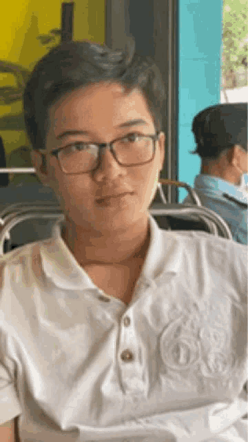 a young man wearing glasses and a white shirt is sitting at a table .
