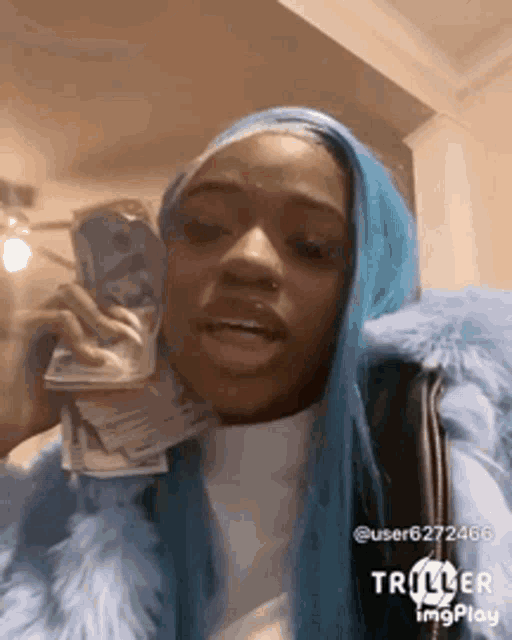 a woman with blue hair is talking on a cell phone while holding a pile of money .